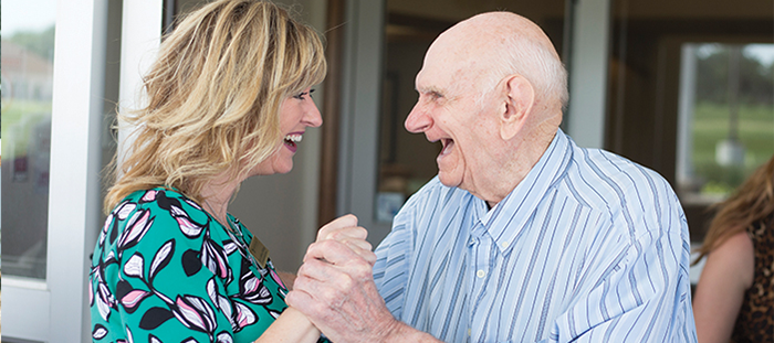 Happy senior man holding hands and smiling with senior living staff member