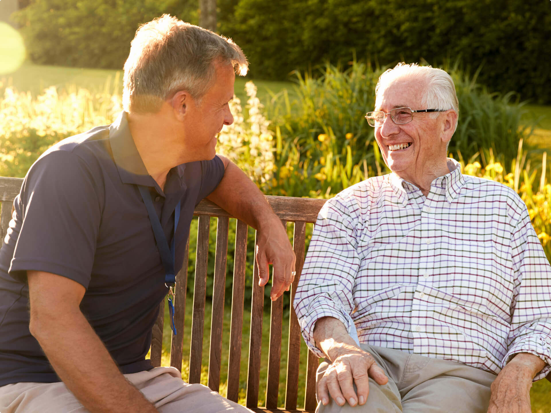 Assisted living resident having conversation with adult son on a bench outside