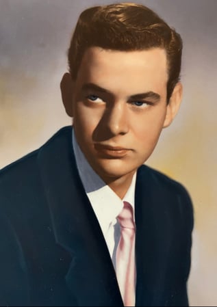 A portrait photo of Cedarhurst Senior Living resident David Arnold as a young man, around the age he was when he played piano at the Hollywood Bowl. The photo is awash with warm colors. David is wearing a suit with a light pink tie.