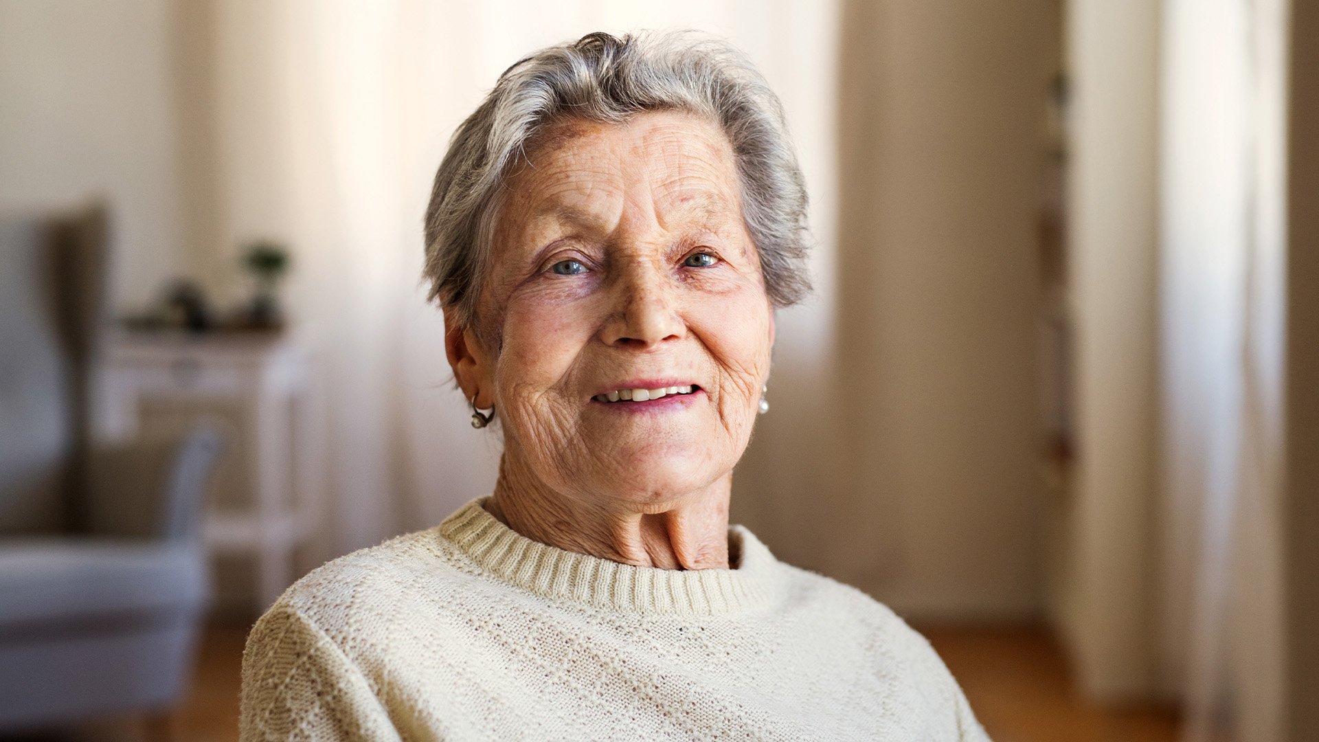 Senior living resident smiling at the camera in a warm and cozy room