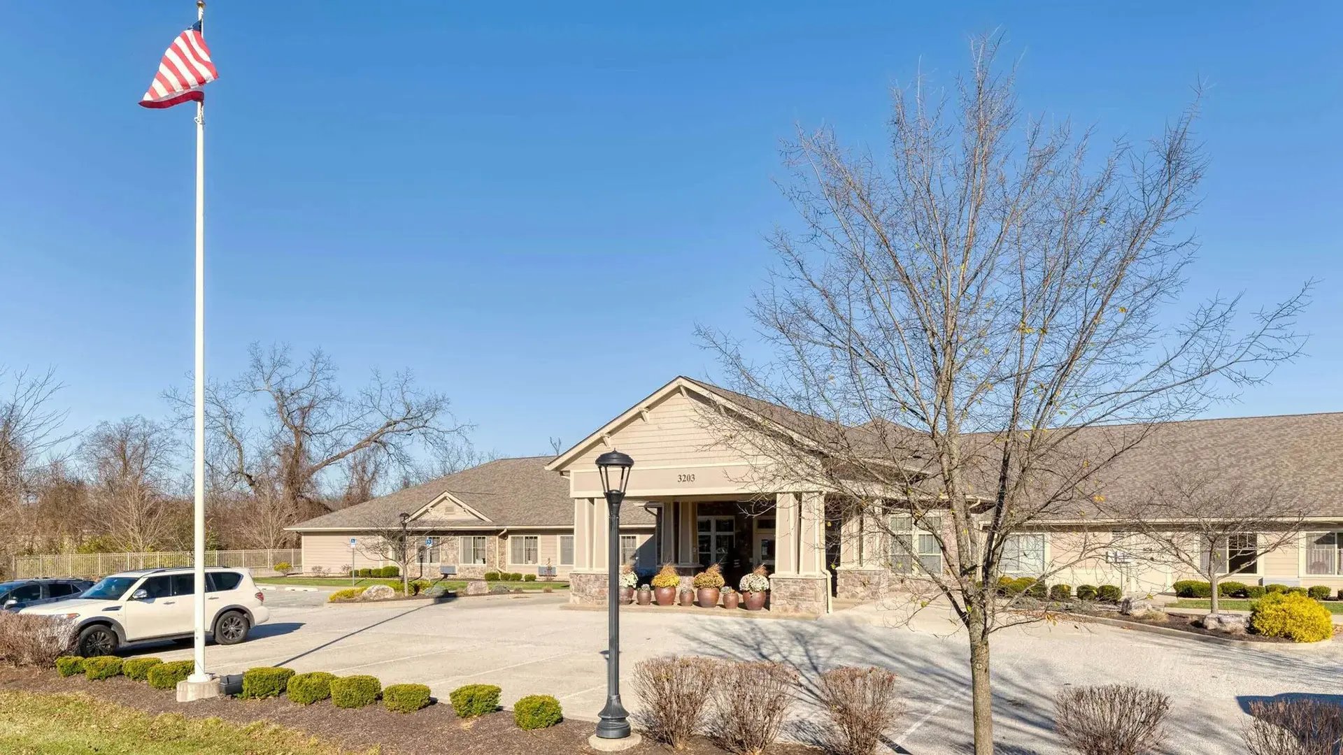 A one-story, beige building with a gabled roof, surrounded by leafless trees and shrubs under a clear blue sky copy