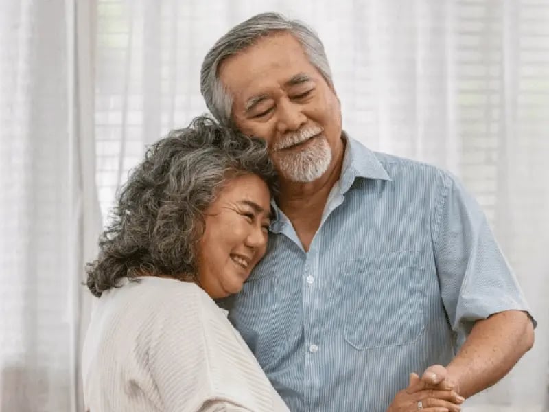 An elderly couple dances closely, smiling warmly