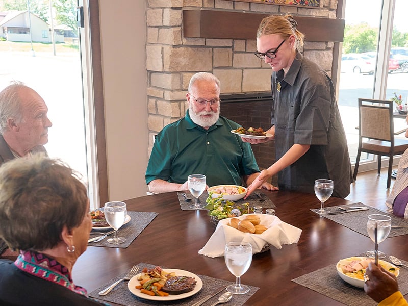 Cedarhurst dining team member serving lunch to a table of senior residents