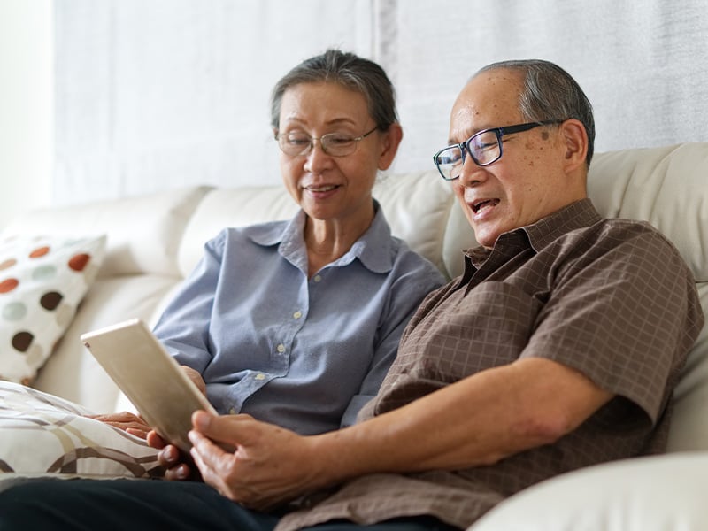 Senior living residents looking together a tablet while happily sitting on the couch