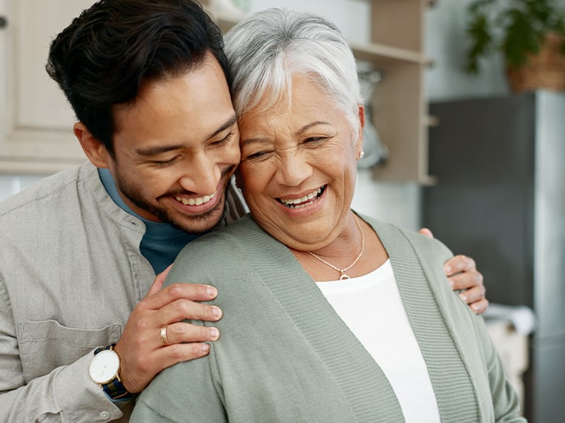 A smiling man embraces an older woman, both showing joy and warmth