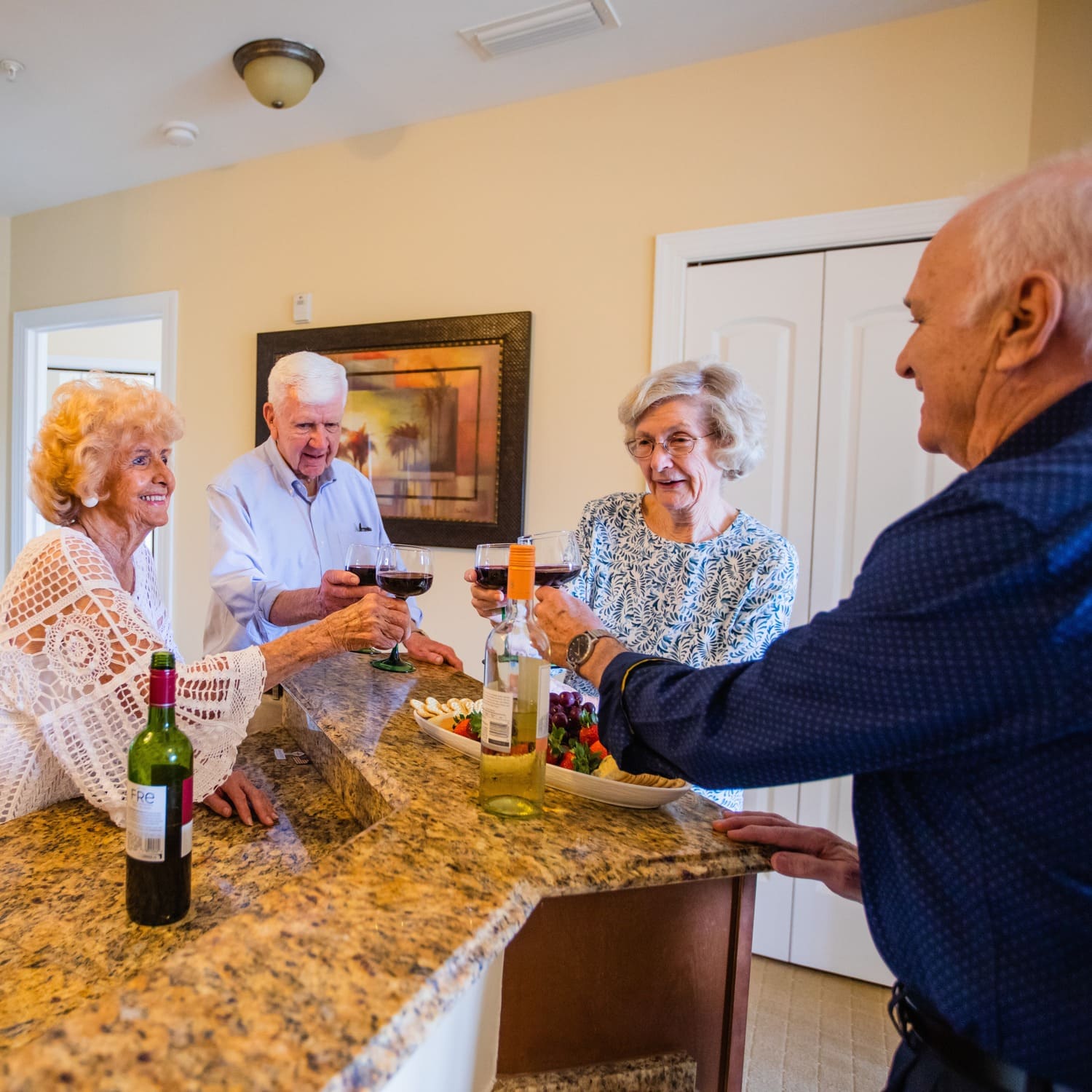 Four senior friends toasting with wine in a kitchen
