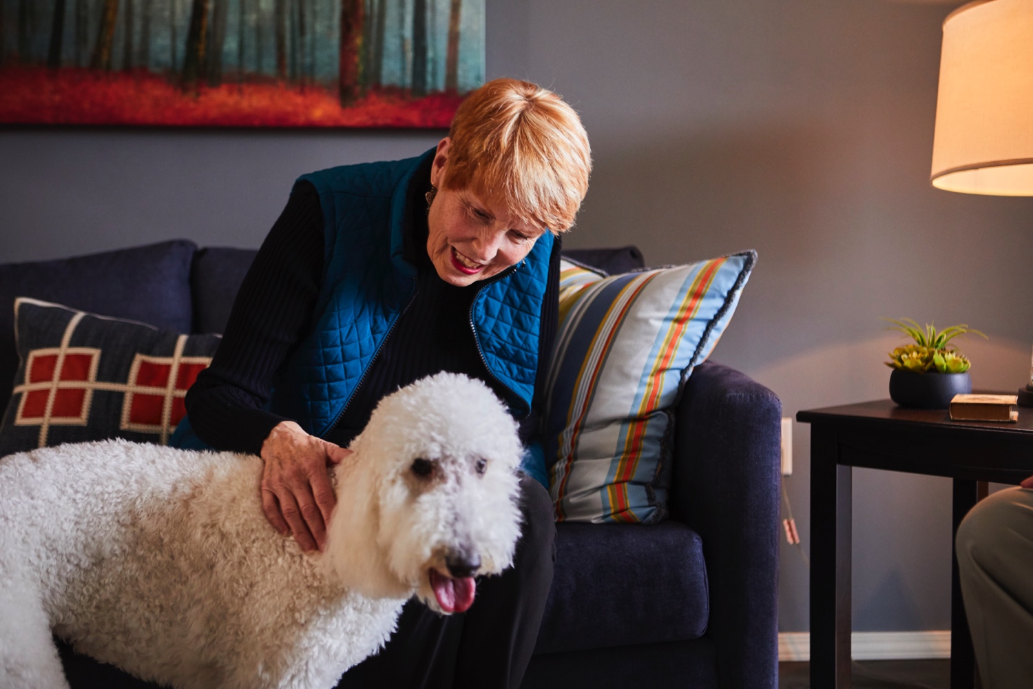 Senior woman sitting on a couch and petting her large white dog