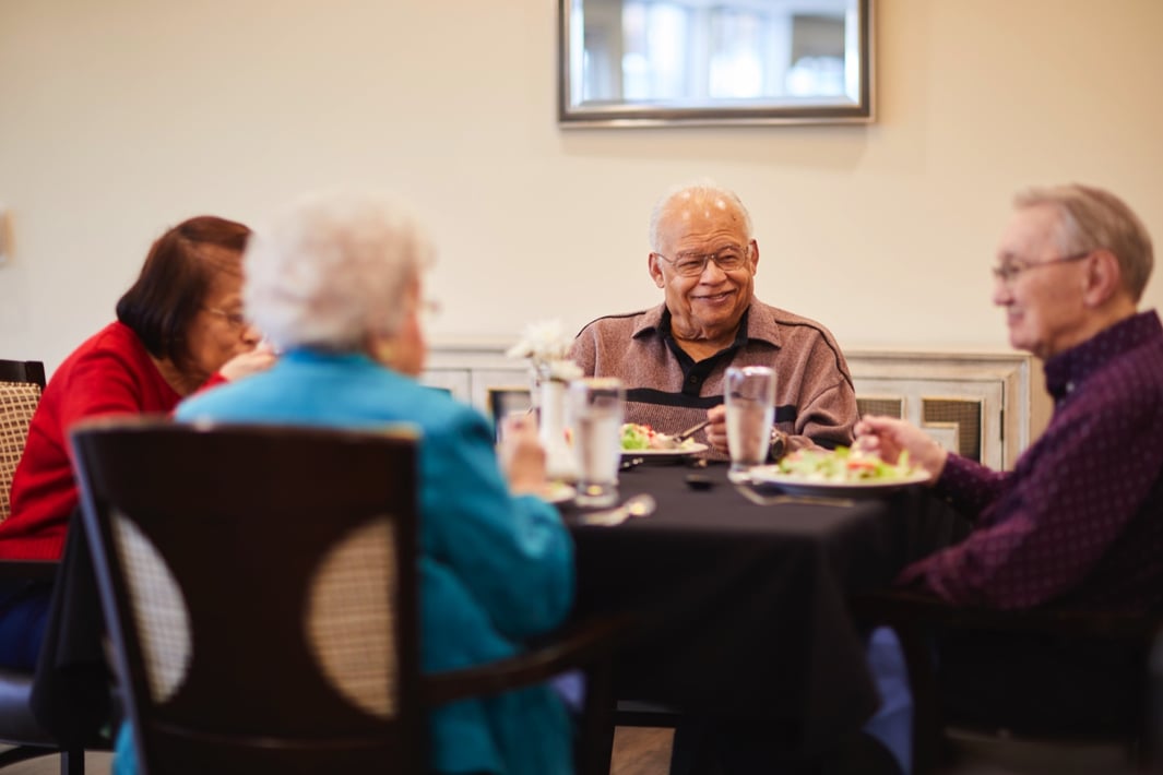 Four senior residents eating lunch at a table in a community dining room
