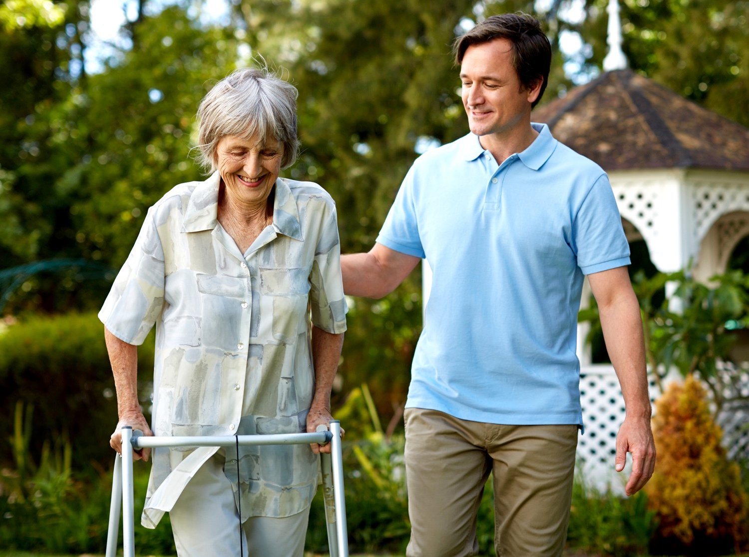 A team member helping a senior woman with a walker in the garden