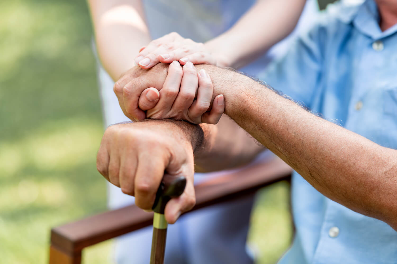 Caregiver holding hand of senior with cane outside