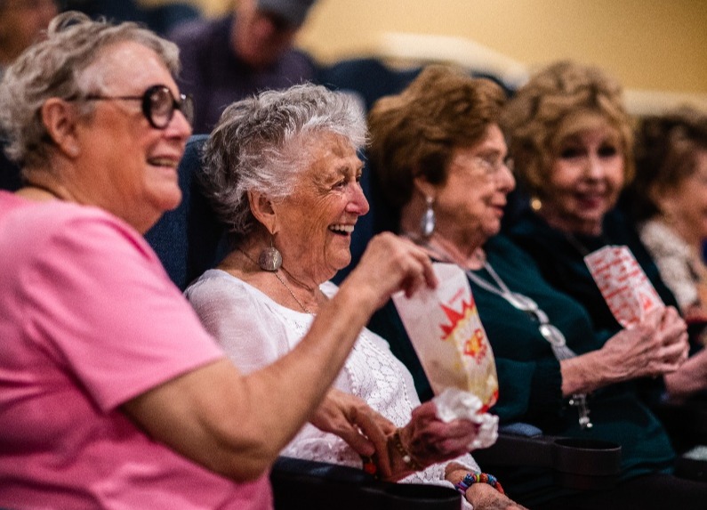 A group of seniors enjoying a movie in the community theater while eating popcorn