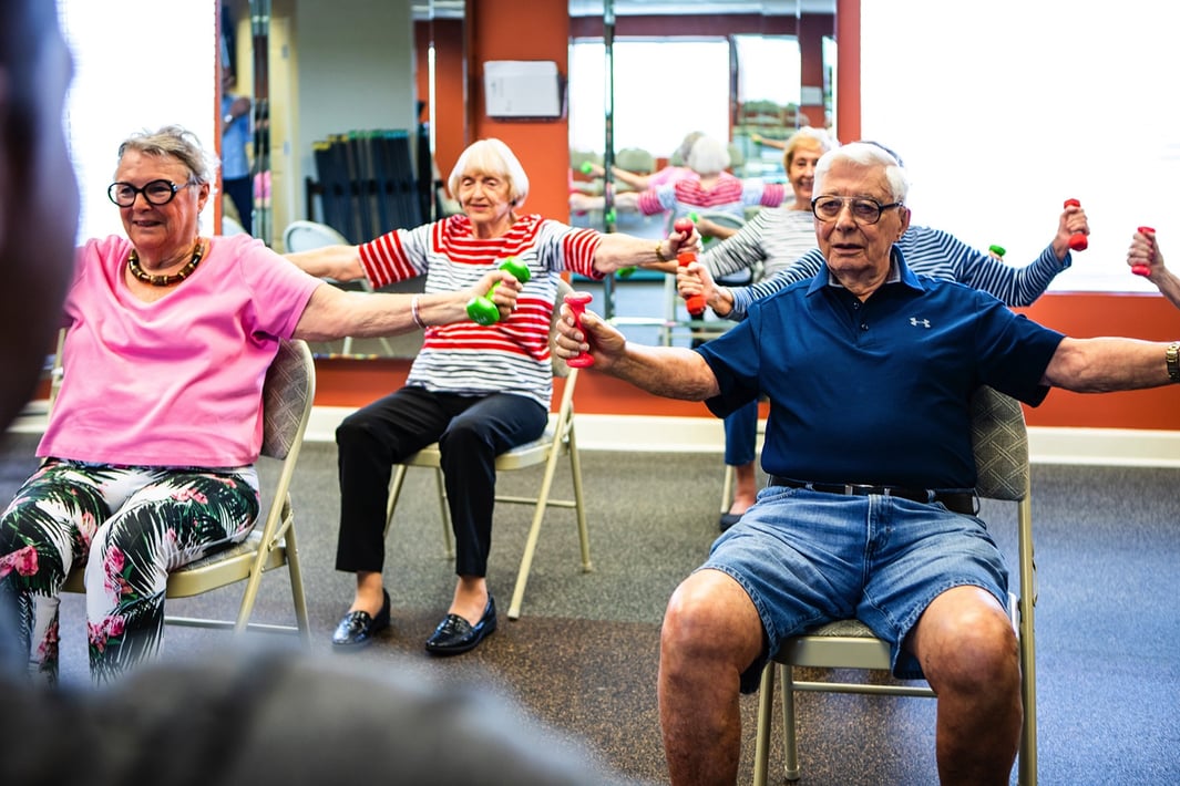 Three seniors participating in a seated fitness class