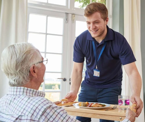 caregiver delivering food to a senior man