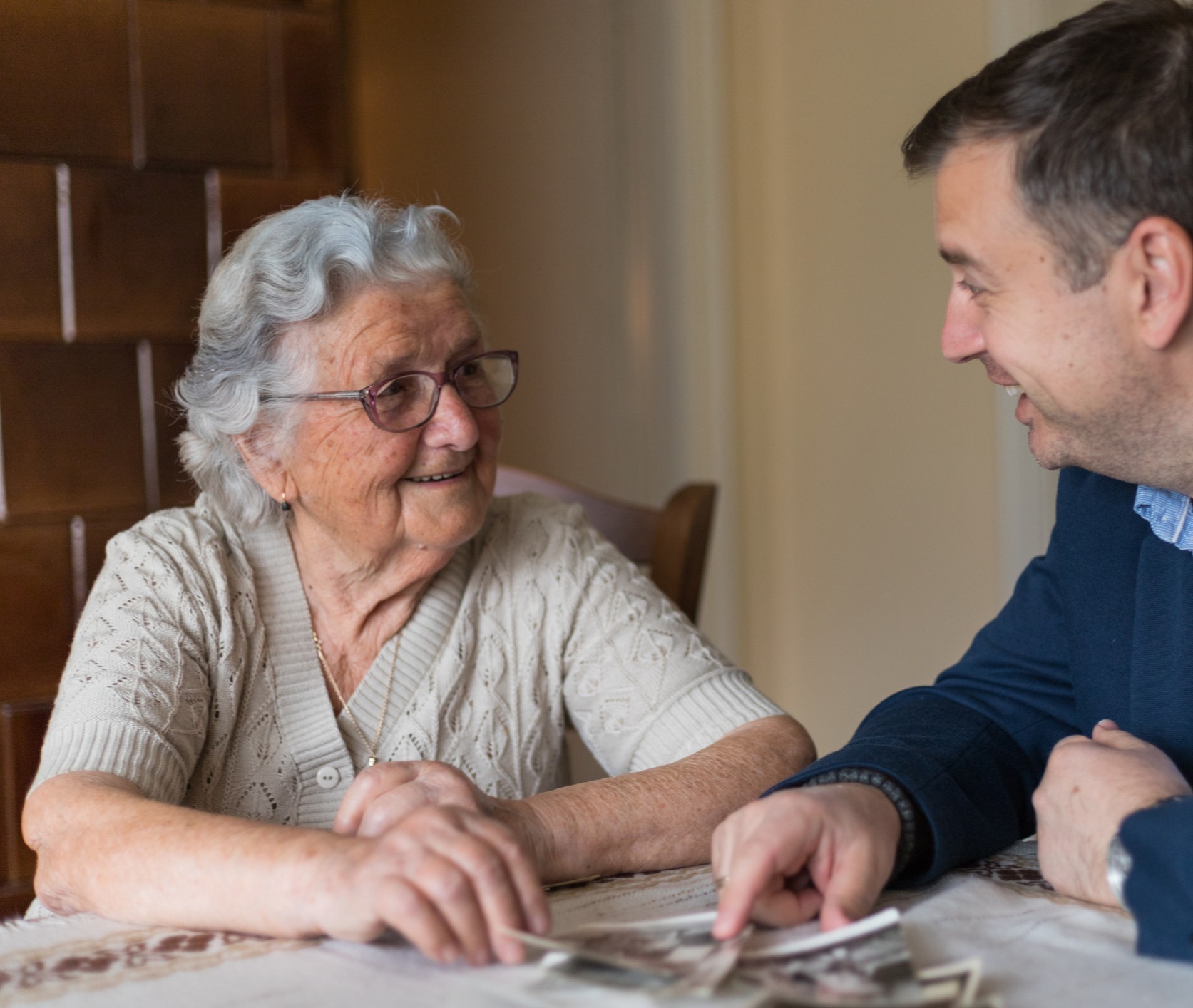 A seated senior woman and younger man looking at a photo album together