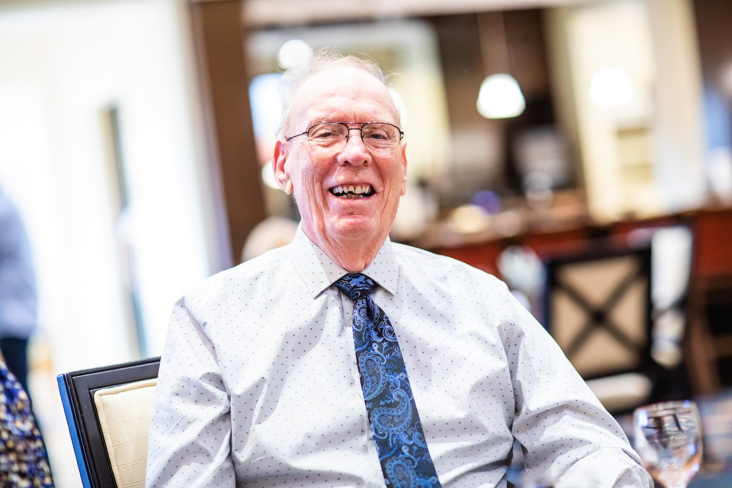 A senior man in a dress shirt and tie smiling at the camera