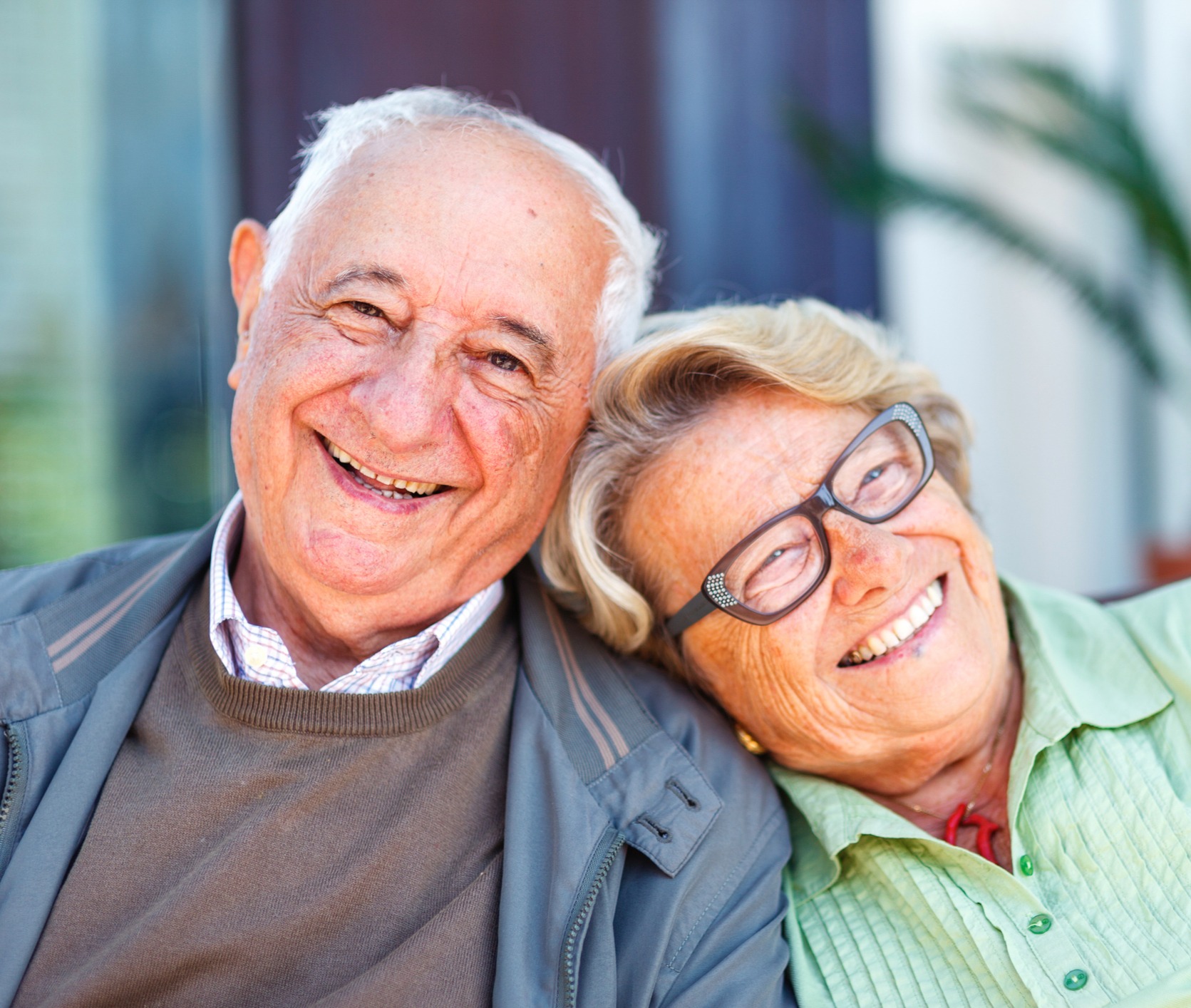 A senior couple, the woman leaning her head on the man's shoulder as they smile at the camera A senior couple, the woman leaning her head on the man's shoulder as they smile at the camera