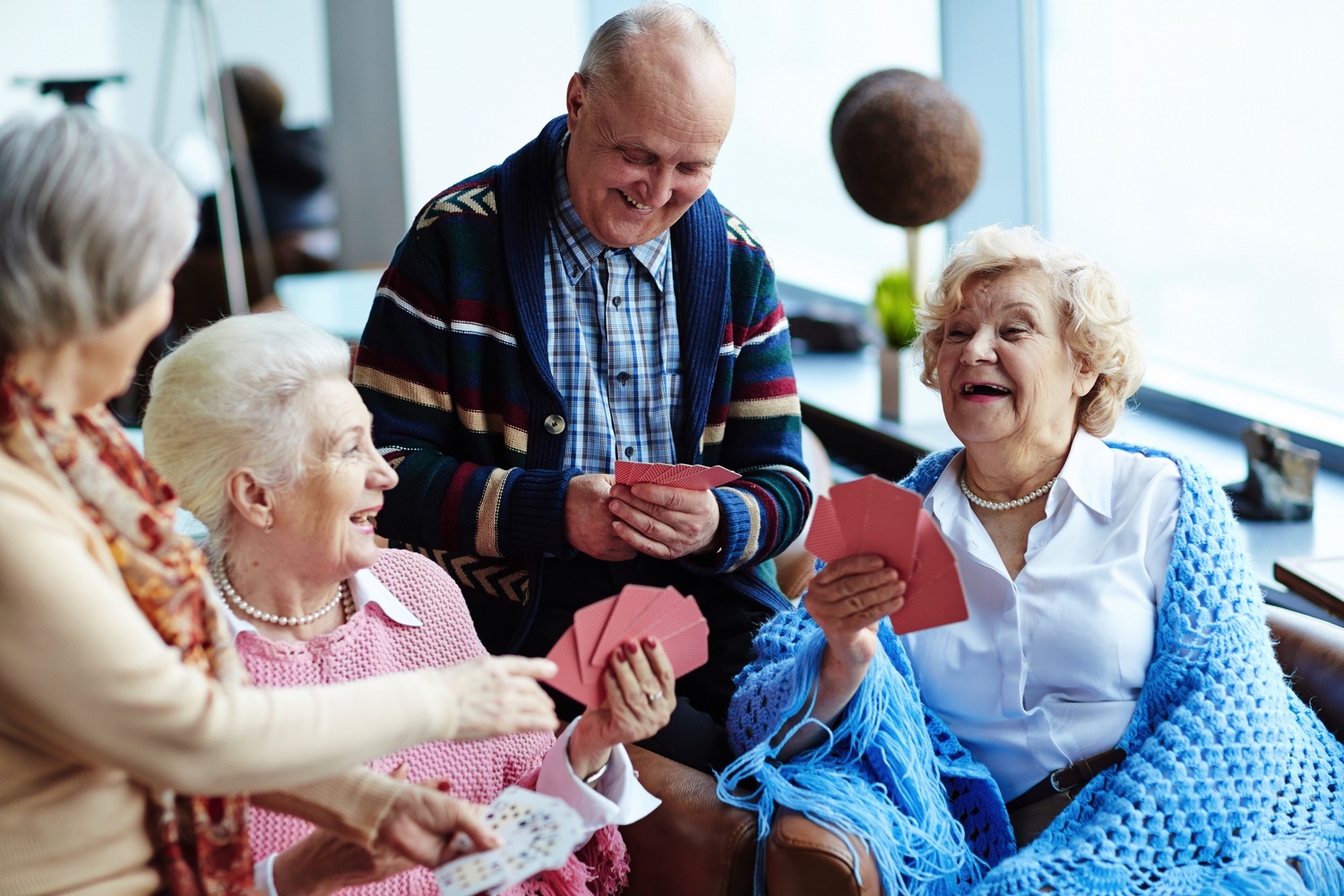 A group of seniors laughing as they play a card game together A group of seniors laughing as they play a card game together