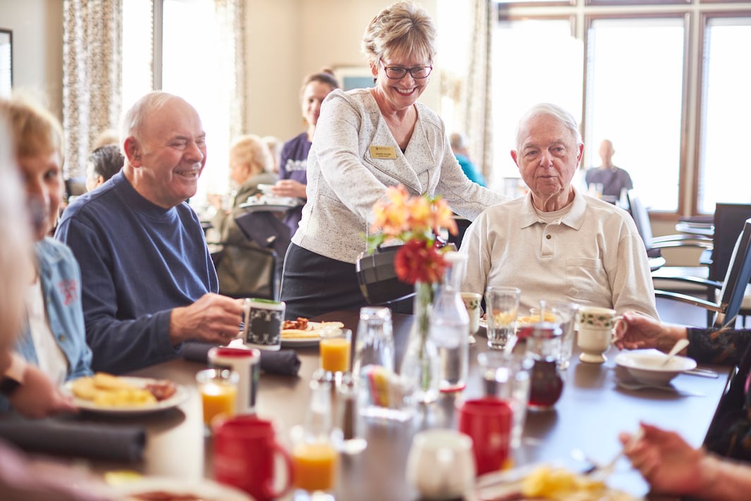 A team member pours coffee for a group of seniors eating breakfast in a community restaurant