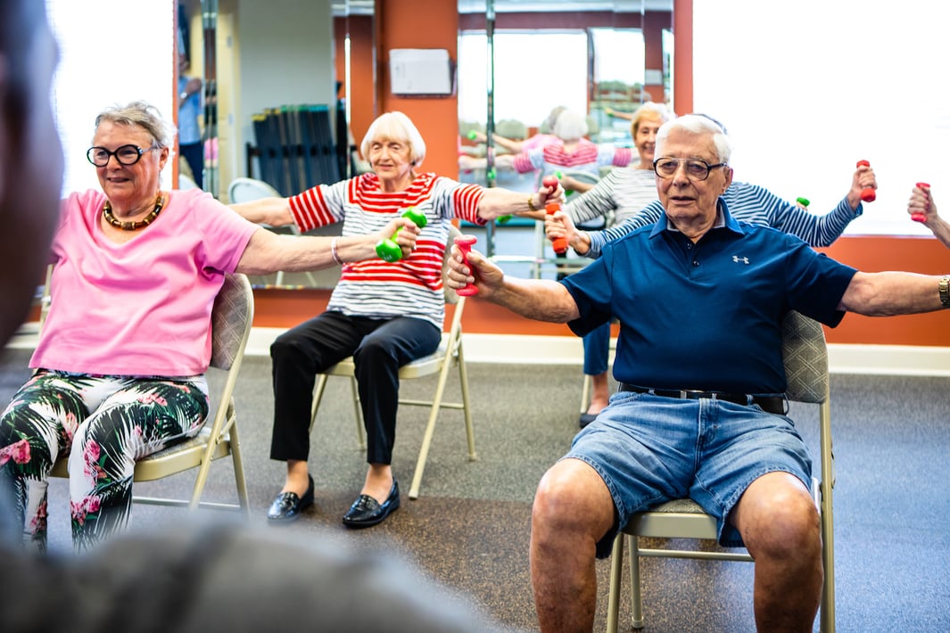 A group of seniors participating in a seated exercise class with hand weights