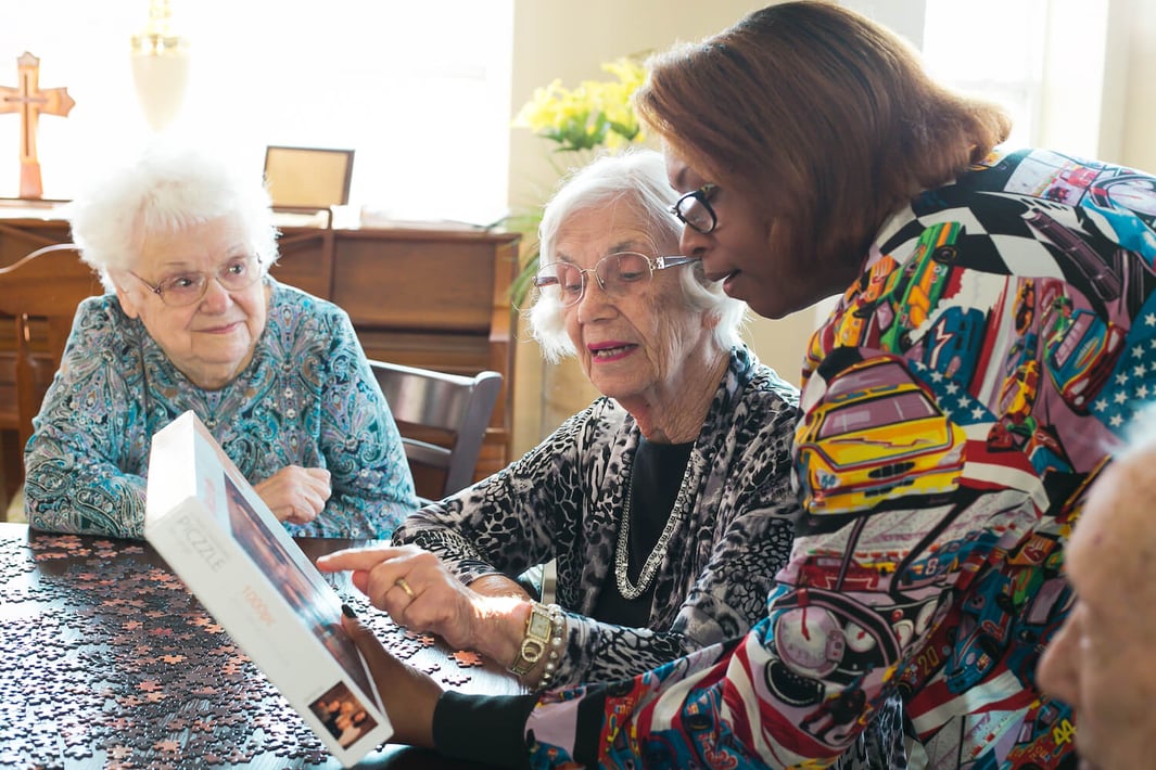 A staff member helping two senior women with a jigsaw puzzle