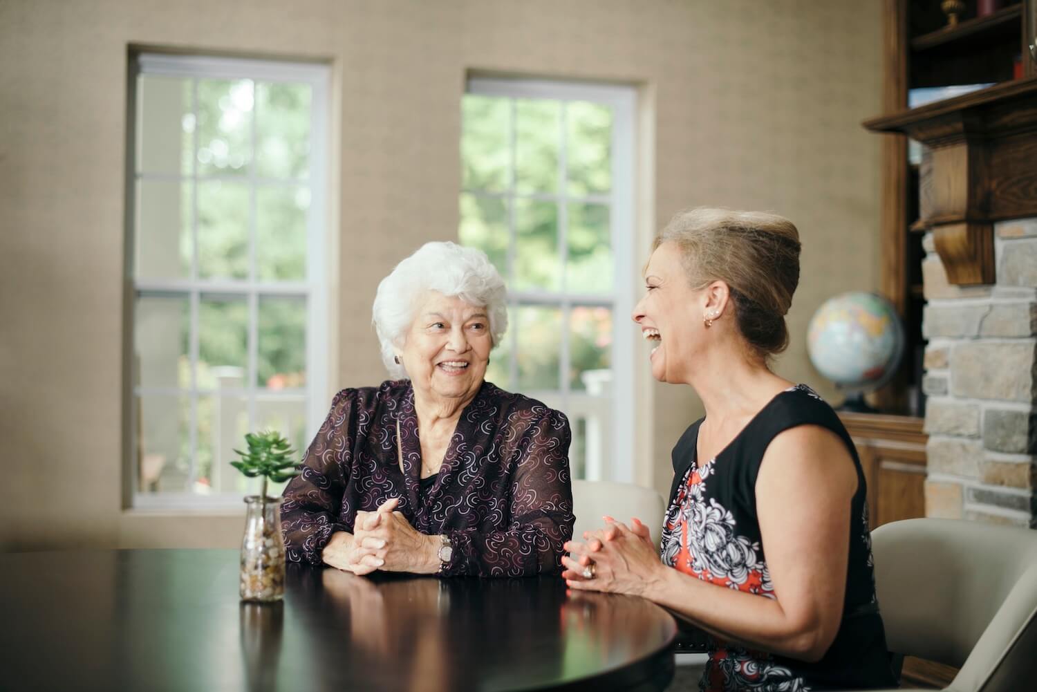 A resident and a caregiver laughing at a dining room table