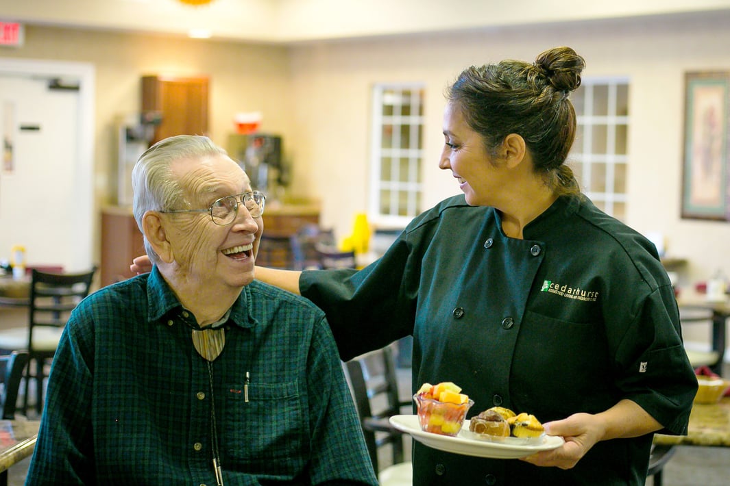 Staff member serving a snack to a senior man in the community restaurant