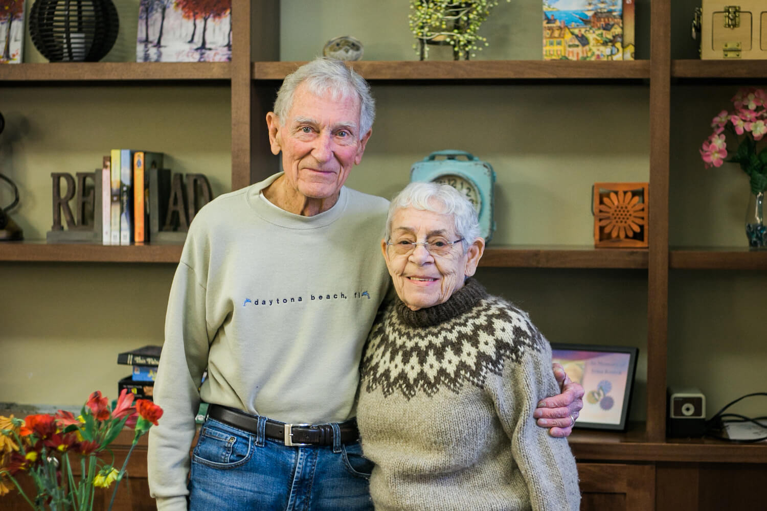 A senior man and woman standing in front of bookshelves, smiling at the camera