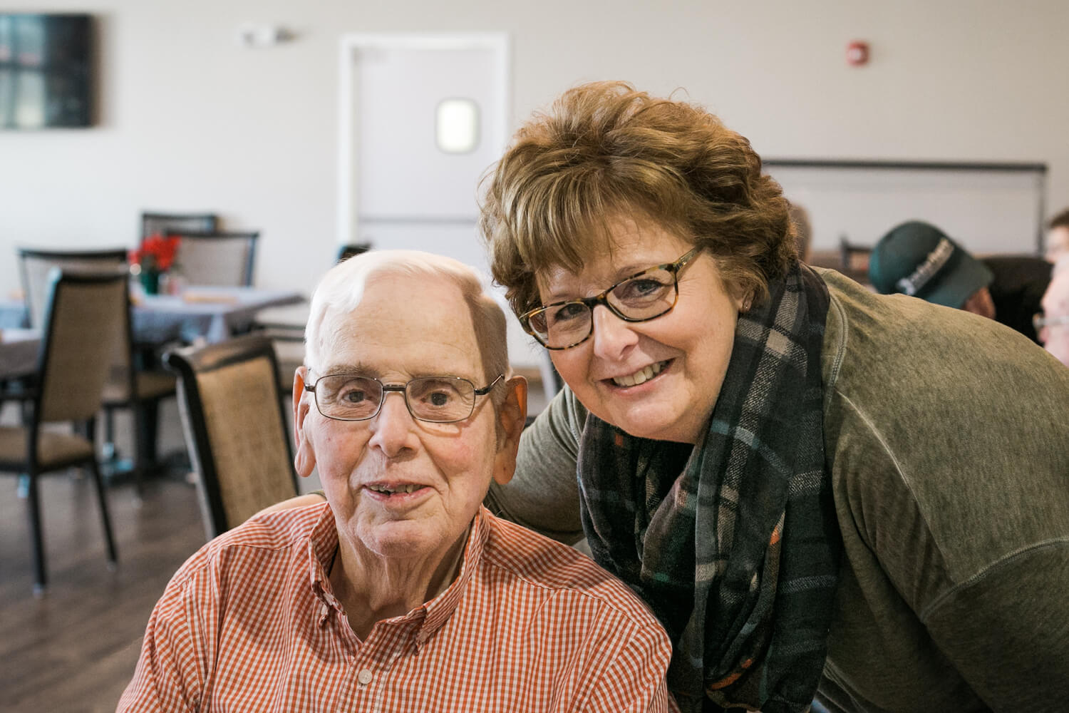 A resident and a caregiver smiling in a dining room