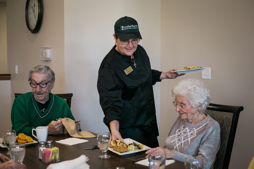 A staff member serving a meal to seniors in the community restaurant