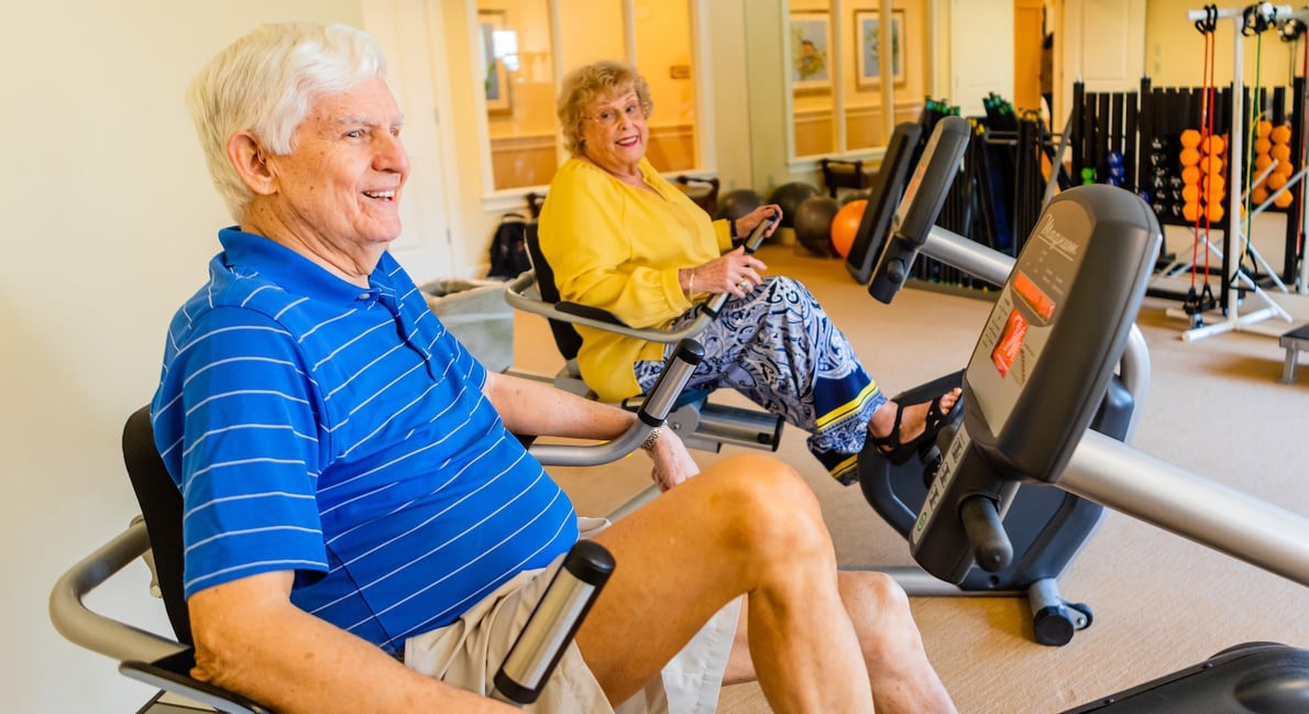 A senior man and woman exercising on stationary bike machines in the gym