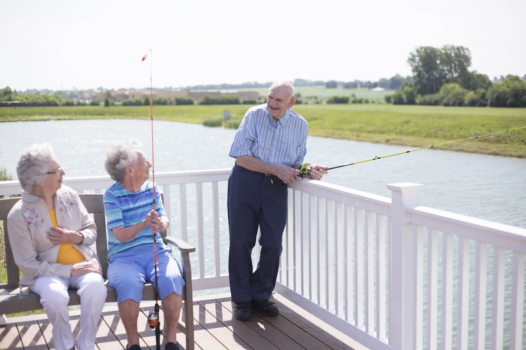 A senior man fishing while two women look on