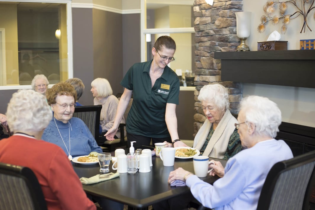 A team member serves a meal to a group of senior residents in the restaurant