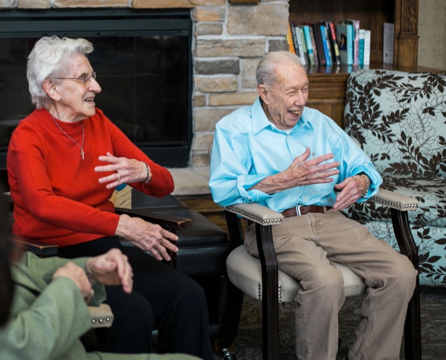 Two senior residents laughing as they sit in the community living room