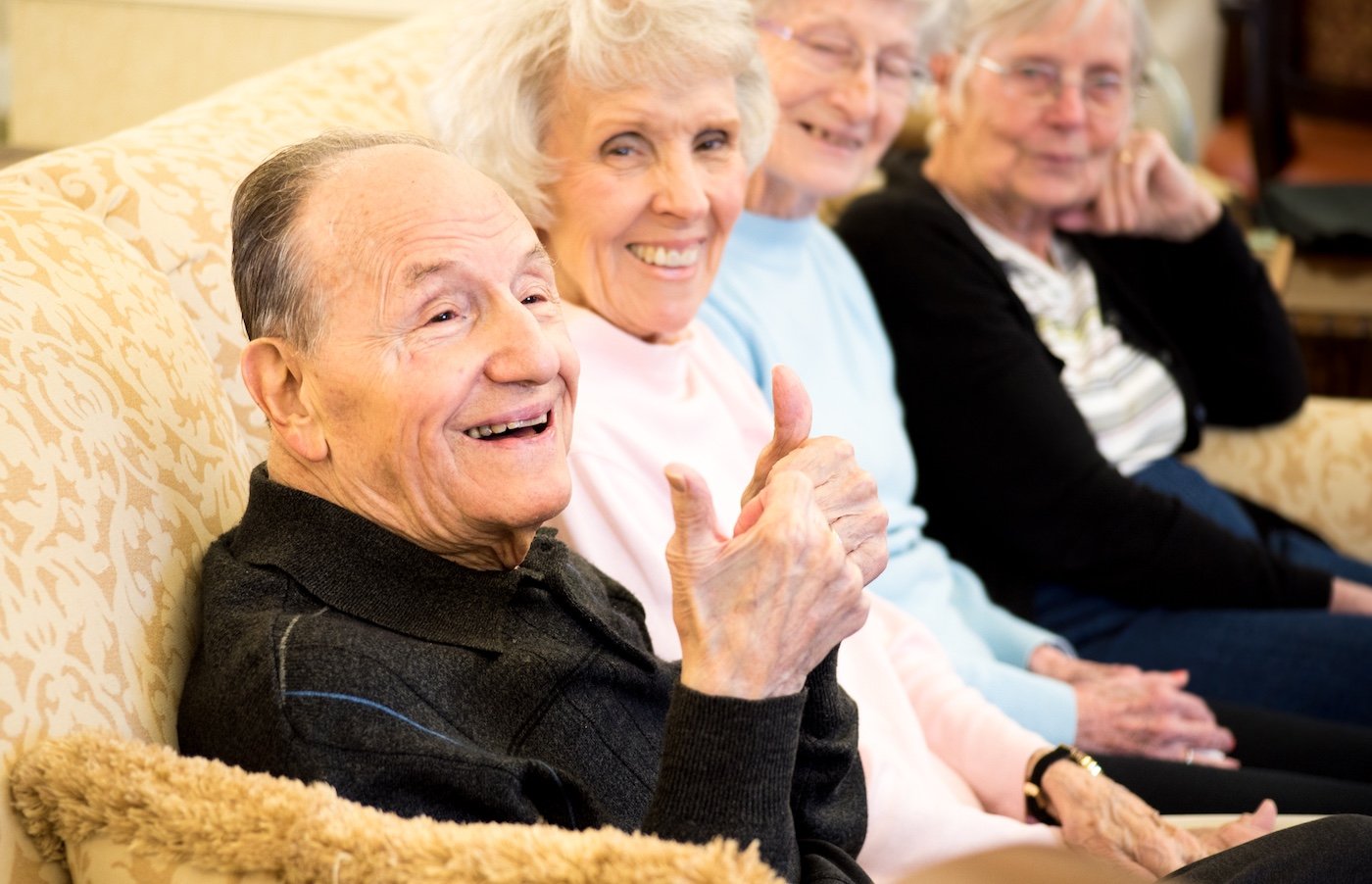 Group of seniors laughing as one man gives a thumbs-up in the foreground