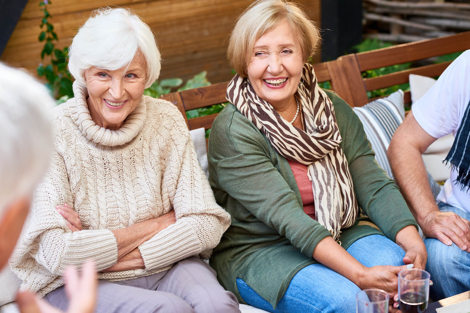 Two senior women laughing while seated on an outdoor bench