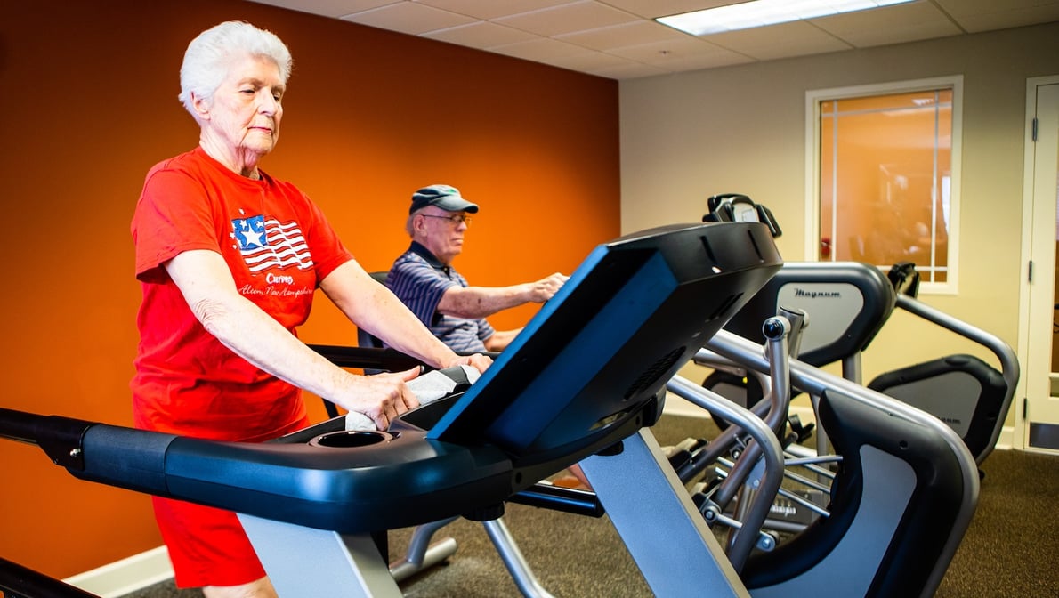 Two seniors exercising on machines in the community gym