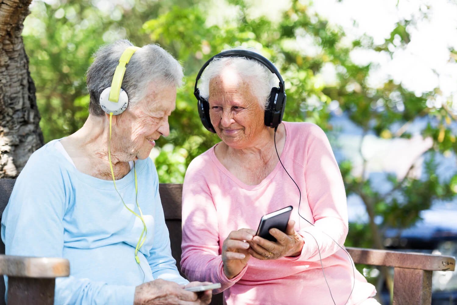Senior women listening to music together on a park bench