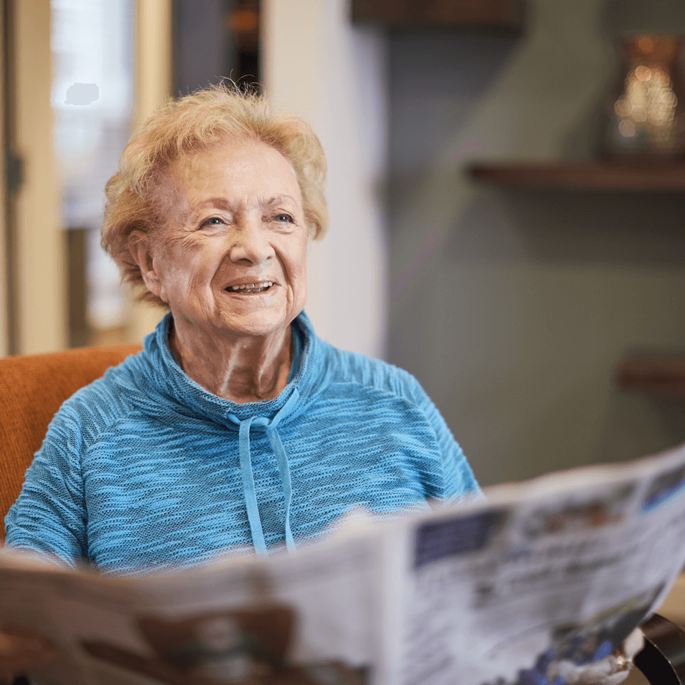 A resident smiling while reading the newspaper 1000 x 1000 (1)