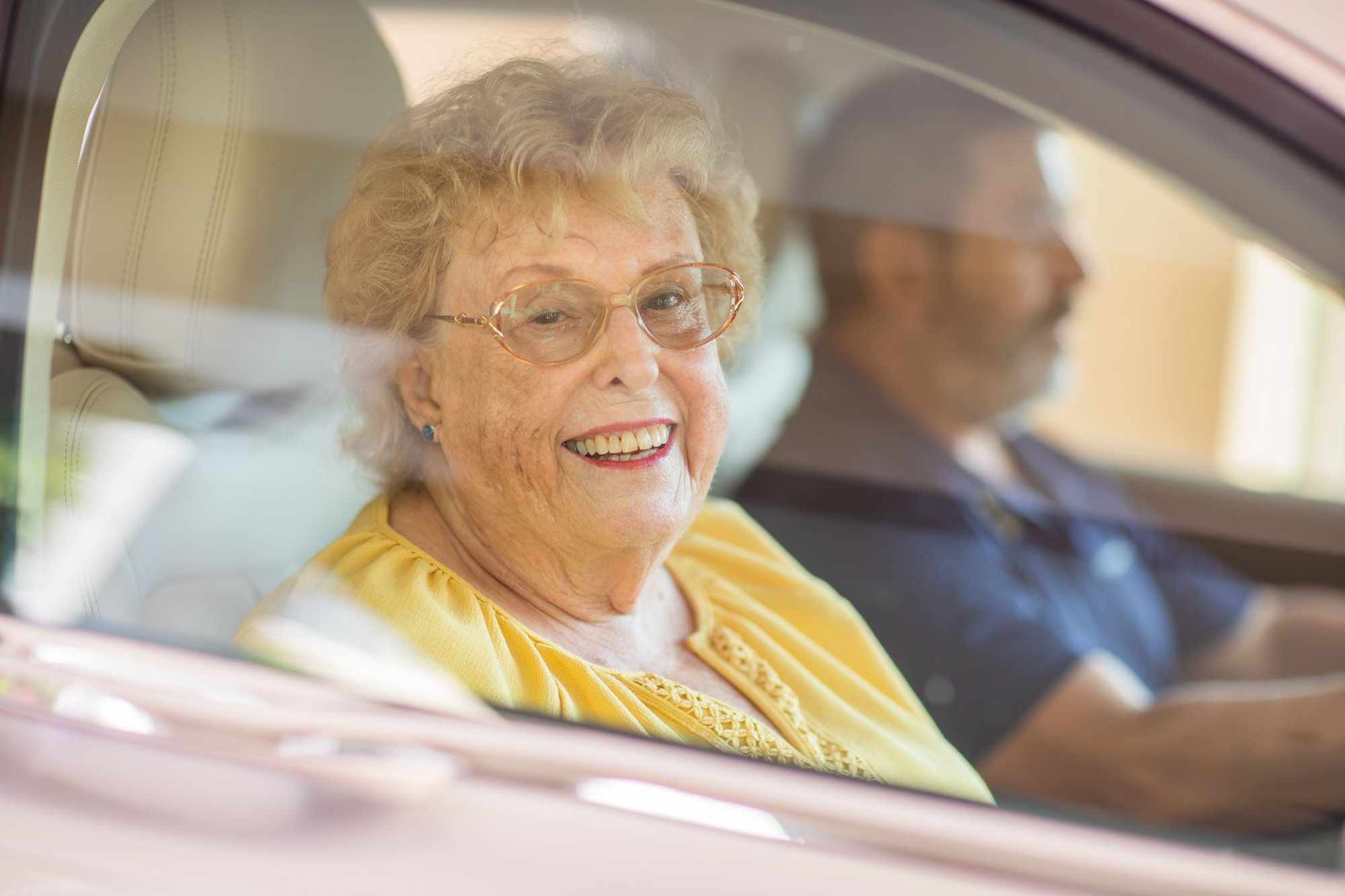 A senior driving with a friend and smiling out of a car window