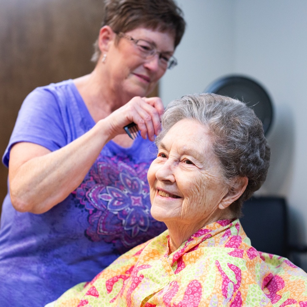 An assisted living caregiver brushes the hair of a senior living resident