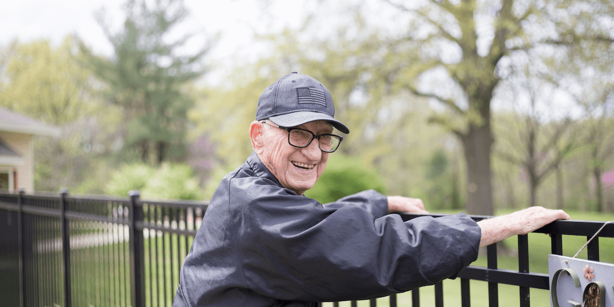 Senior man smiling as he leans against a fence