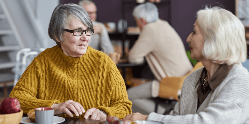 Two senior living residents chatting in common room area