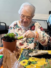 A senior woman puts fresh soil in a small gardening pot.