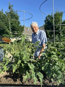 A senior man stands in a garden smiling. His face is framed perfectly in between two vertical planters.