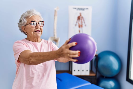 Woman in senior living lifting a purple weighted ball in physical therapy.