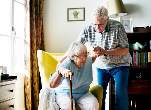 Older man helping senior parent get out of a chair at home