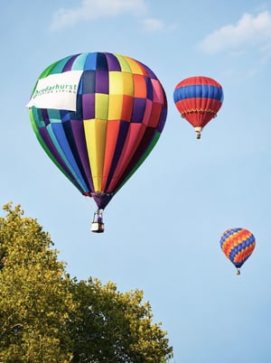 A hot air balloon with a logo for Cedarhurst Senior Living soars through the air.