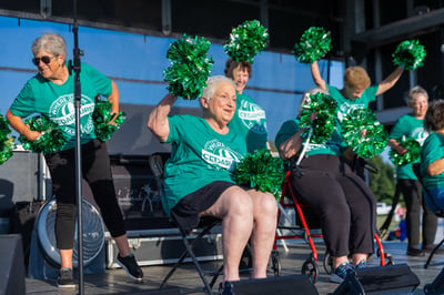 Senior living residents performing cheers on stage at an event.