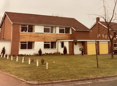 A sepia-toned photo from the 1980s of a woman standing in front of an old British house named 'Pengwern'