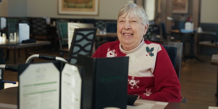 A senior woman sits in the dining room of a senior living community, looking over a menu.